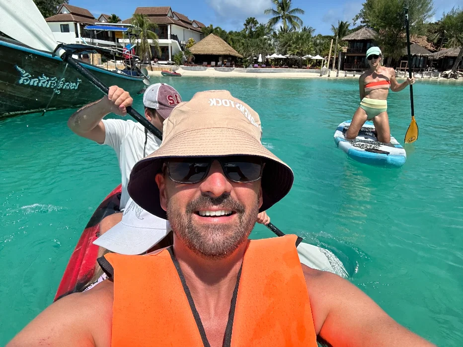 Two kayakers paddling out from Sunrise Beach, Koh Lipe, with the small uninhabited islands offshore visible in the distance