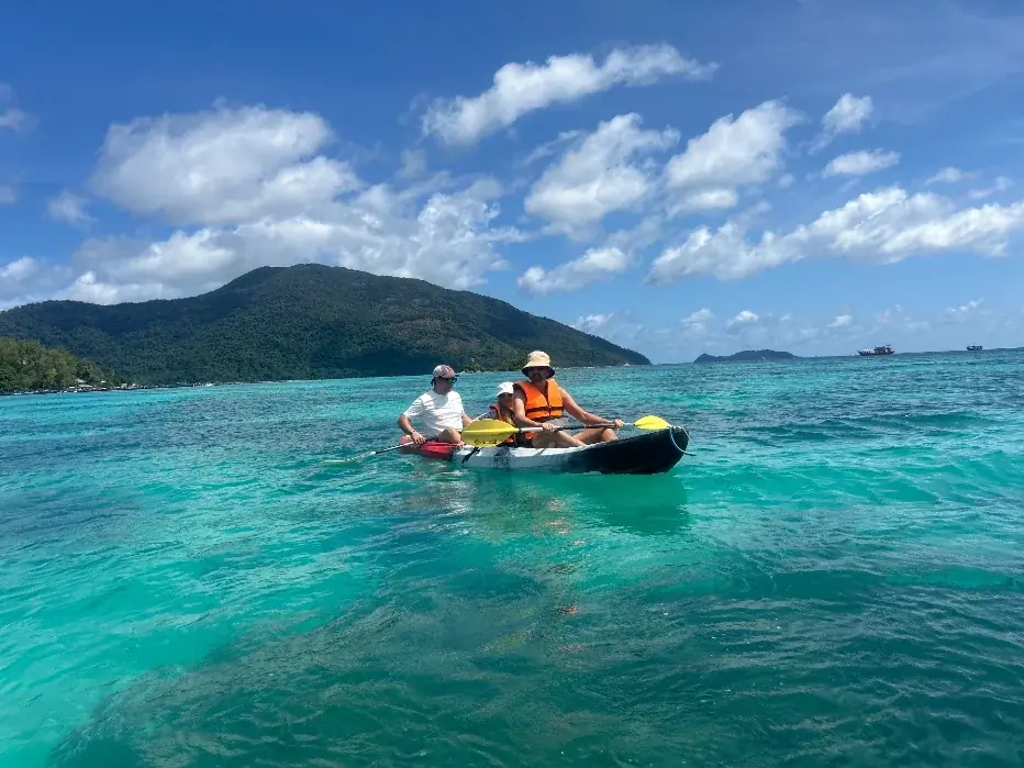 Two people kayaking from Sunrise Beach toward a small island offshore, with Koh Adang in the background